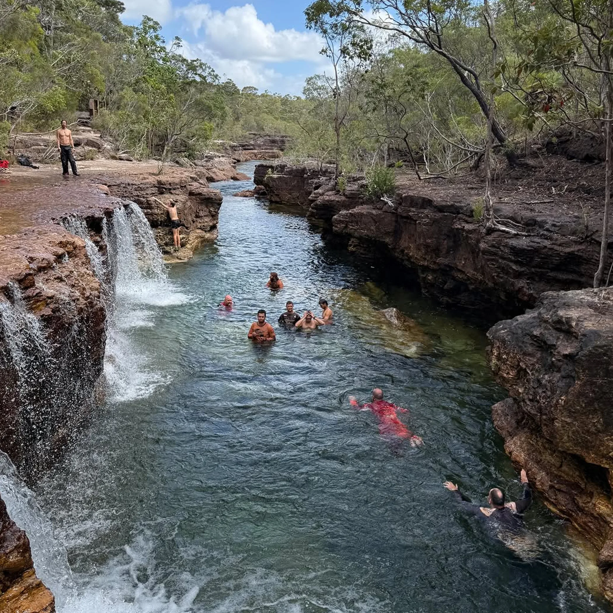 people swimming in a natural waterfall pool